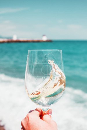 Photo for Woman hand with white wine glass on a turquoise Mediterranean sea foam, waves and beach background. Summer vacation in Europe. Nice, French riviera. Alcohol drink photo. - Royalty Free Image
