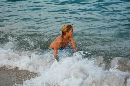 Ein blonder Junge spielt in den Wellen mit einem Schwimmbrett
