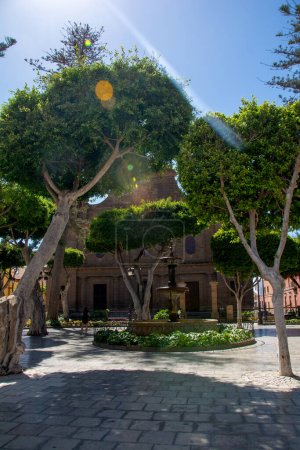 Bäume mit Blick auf einen Brunnen und die Kirche von Santiago de los Caballeros in der Stadt Galdar auf der Kanarischen Insel Gran Canaria, Europa