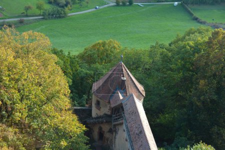 Blick von oben auf das Dach einer alten Burg und eine grüne Landschaft mit Wiese und Baum