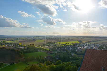 Blick von oben auf das Dach einer alten Burg und eine grüne Landschaft mit Häusern eines Dorfes, Ackerland, Wald und blauem Himmel