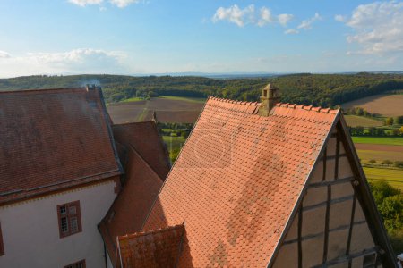 Blick von oben auf das Dach einer alten Burg und eine grüne Landschaft mit Ackerland, Wald und blauem Himmel