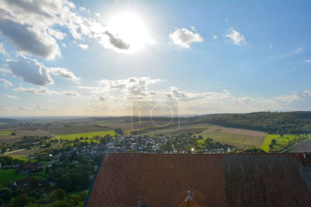 Blick von oben auf das Dach einer alten Burg und eine grüne Landschaft mit Häusern eines Dorfes, Ackerland, Wald und blauem Himmel