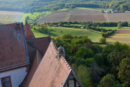 Blick von oben auf das Dach einer alten Burg und eine grüne Landschaft mit Ackerland, Wald und blauem Himmel