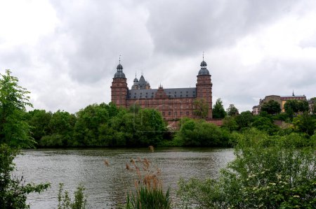View of Johannisburg Castle in Aschaffenburg with a river and a cloudy sky