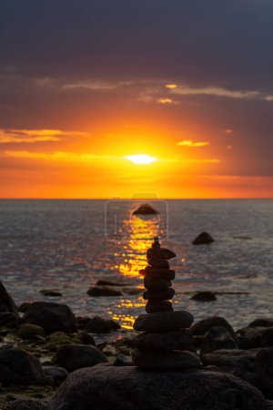 Gestapelte Steine an einem Strand an der Ostseeküste bei orangefarbenem Sonnenuntergang