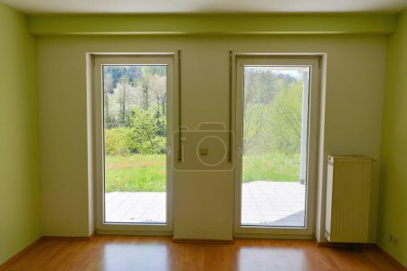 Two patio doors in an empty, freshly painted room with a view of green nature