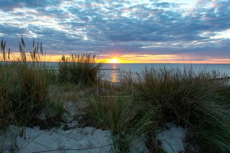Coucher de soleil sur la mer, avec dunes de sable, herbe de plage et brise-lames
