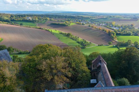 Vue de dessus sur le toit d'un ancien château et un paysage verdoyant avec des maisons d'un village, terres agricoles, forêt et ciel bleu
