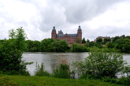 View of Johannisburg Castle in Aschaffenburg with a river and a cloudy sky