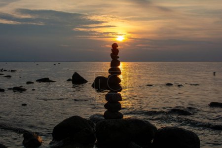 Pierres empilées sur une plage sur la côte de la mer Baltique au coucher du soleil orange