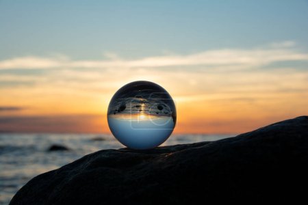 Bola de vidrio en una roca al atardecer en la playa, el mar y el sol poniente se reflejan en la pelota