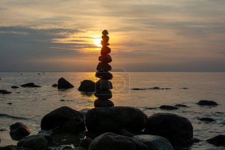 Gestapelte Steine an einem Strand an der Ostseeküste bei orangefarbenem Sonnenuntergang