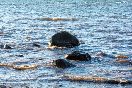 Big stones lie in the water on the Baltic Sea coast, with waves