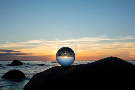 Bola de vidrio en una roca al atardecer en la playa, el mar y el sol poniente se reflejan en la pelota