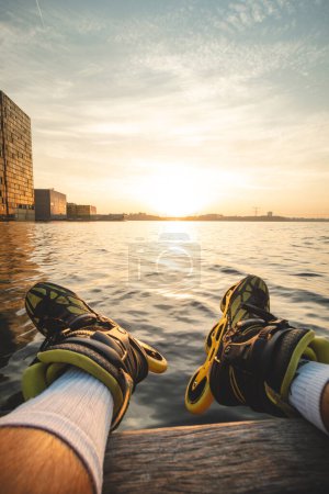 Photo for Athlete sits on a wooden pier after a roller skating ride and watches the sunset in Almere, Netherlands. - Royalty Free Image