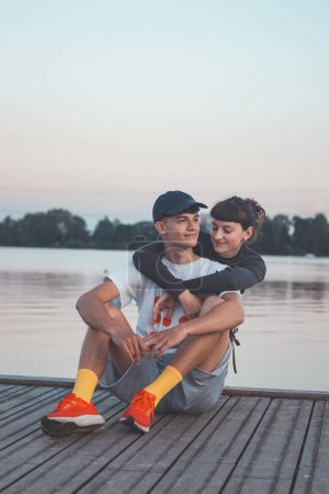 Photo for Cute young couple on the shore of a lake looking into their future during sunset. 20-year-old couple hugging. - Royalty Free Image