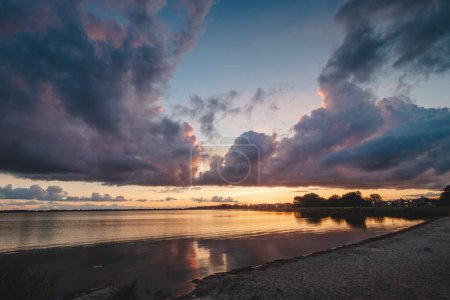Photo for Perfect sunset on the shores of Lake Gooimer near Almere. The purple-orange inferno illuminates the passing clouds and reflects on the calm surface. Beauty of Netherlands. - Royalty Free Image