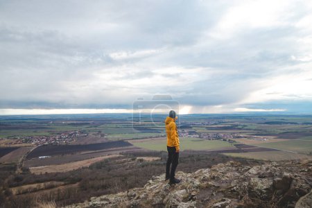 Traveller in a yellow jacket stands on top of Mount Rip and is pointing at the city of Prague. Exploring the Czech country.