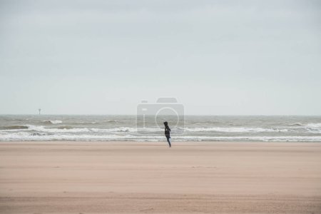 Man walks on a sandy beach in the face of high winds near Blankenberge, west coast of Belgium. Exploring and discovering Belgium.
