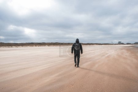 Man walks on a sandy beach in the face of high winds near Blankenberge, west coast of Belgium. Exploring and discovering Belgium.