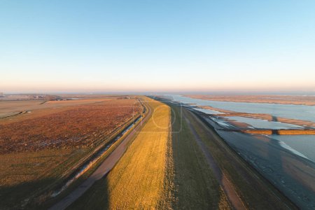 Embankment protege a los residentes en el sur de los Países Bajos del agua del océano bajo un brillante amanecer amarillo anaranjado. Impresionante mañana.