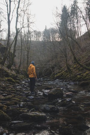 Téléchargez les photos : Un jeune homme vêtu d'une veste orange se détend dans le courant d'une rivière de la région wallonne de Belgique. Reflet d'un homme dans l'eau de la rivière. Découvrir la faune sauvage en Belgique. - en image libre de droit