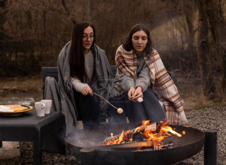 young women are roasting marshmallows on a fire outdoors