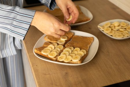 female hands, young woman puts banana slices on peanut butter toast