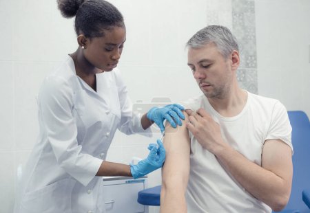 Téléchargez les photos : African-American female doctor gives an injection inoculation in the arm of a male patient - en image libre de droit