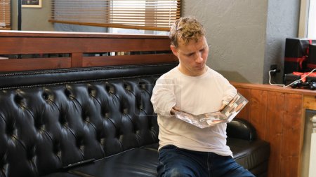 Foto de Un joven con discapacidad está mirando un catálogo al elegir un peinado en una peluquería. - Imagen libre de derechos