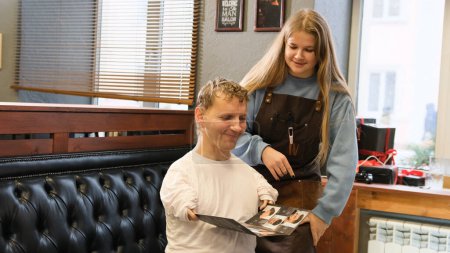 Téléchargez les photos : Un jeune homme handicapé discute d'une coupe de cheveux avec son maître dans un salon de coiffure. - en image libre de droit