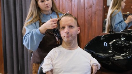 Téléchargez les photos : Une coiffeuse dans un salon de beauté fait une coupe de cheveux et coiffure pour un homme handicapé - en image libre de droit