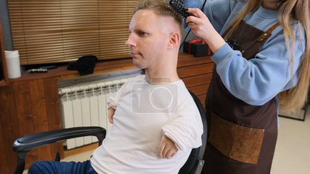 Téléchargez les photos : Une coiffeuse dans un salon de beauté fait coiffure pour un homme handicapé - en image libre de droit
