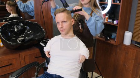 Foto de Una peluquera en un salón de belleza peina el cabello de un hombre con discapacidad - Imagen libre de derechos