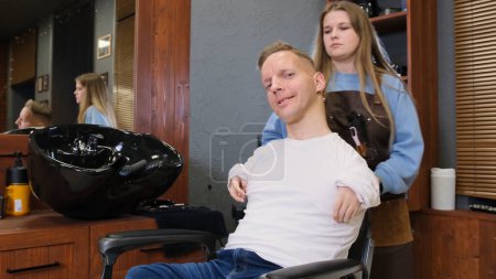 Téléchargez les photos : Un homme handicapé dans un T-shirt blanc fait une coupe de cheveux et coiffure dans un salon de coiffure. Une vie pleine pour les personnes handicapées. - en image libre de droit