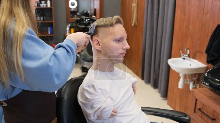 Foto de Un hombre con discapacidades en una camiseta blanca hace un corte de pelo y peinado en una peluquería. Una vida plena para las personas con discapacidad. - Imagen libre de derechos