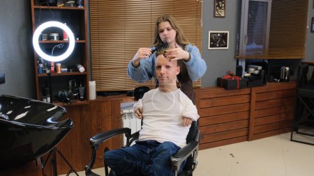 Téléchargez les photos : Un homme handicapé dans un T-shirt blanc fait une coupe de cheveux et coiffure dans un salon de coiffure. Une vie pleine pour les personnes handicapées. - en image libre de droit