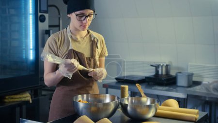 Téléchargez les photos : Une pâtissière dans la cuisine remplit de crème anglaise de crème au beurre à l'aide d'un sac à pâtisserie - en image libre de droit