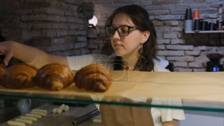 Téléchargez les photos : La vendeuse met des croissants à vendre sur la fenêtre de la boulangerie - en image libre de droit