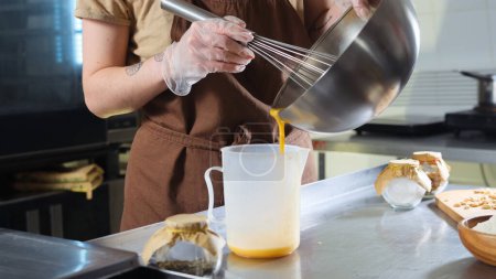 Foto de Verter el líquido de los huevos batidos en un tazón grande Las cocineras preparan un producto culinario o masa. - Imagen libre de derechos