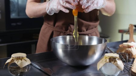 Téléchargez les photos : Une cuisinière dans la cuisine d'un restaurant brise un œuf dans un bol en métal - en image libre de droit