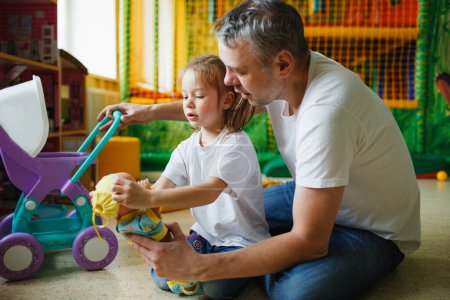 Foto de Una chica feliz con su padre juega con muñecas en un centro de juegos para niños. - Imagen libre de derechos
