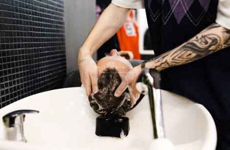 Téléchargez les photos : Un coiffeur lave la tête d'un homme dans un salon de coiffure. Salon de coiffure professionnel pour hommes. Salon de coiffure. - en image libre de droit