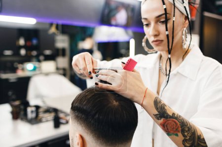 Téléchargez les photos : Une coiffeuse coupe les cheveux d'un homme dans un salon de coiffure. Salon de coiffure professionnel pour hommes. Salon de coiffure - en image libre de droit
