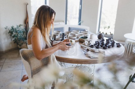 Téléchargez les photos : Une jeune femme sculpte à partir d'argile dans son atelier de poterie. Travaux de poterie. Création de produits en argile - en image libre de droit