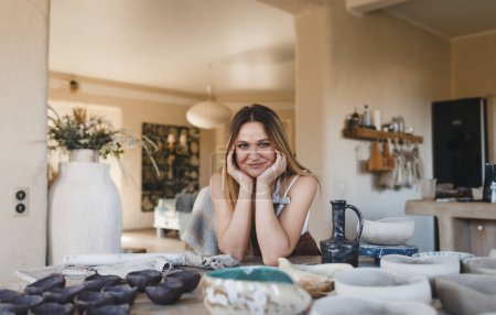 Téléchargez les photos : Une jeune femme sculpte de l'argile dans son atelier de poterie assis à une table. Travaux de poterie. Création de produits en argile - en image libre de droit