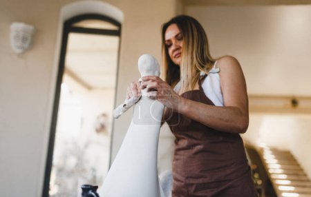 Téléchargez les photos : Une femme travaille sur une statue dans son atelier de poterie. Travaux de poterie. Création de produits en argile. - en image libre de droit