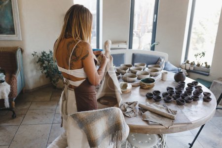 Téléchargez les photos : Une jeune femme travaille dans son atelier de poterie. Travaux de poterie. Création de produits en argile. - en image libre de droit