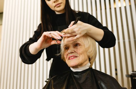 Téléchargez les photos : Portrait d'une femme âgée visitant un coiffeur professionnel. Un coiffeur expérimenté fait coiffure pour un client - en image libre de droit
